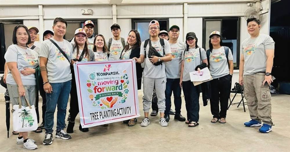 Nonpareil volunteers posing indoors with Moving Forward and Giving Back tree planting banner
